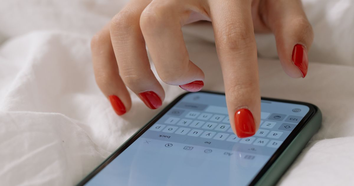 Close-up of a manicured hand using a free nail photo editing app on a smartphone