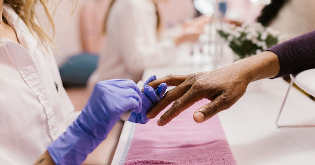 Close-up of a manicurist polishing a client's nails in a salon, the gap where nail photos get edited between clients