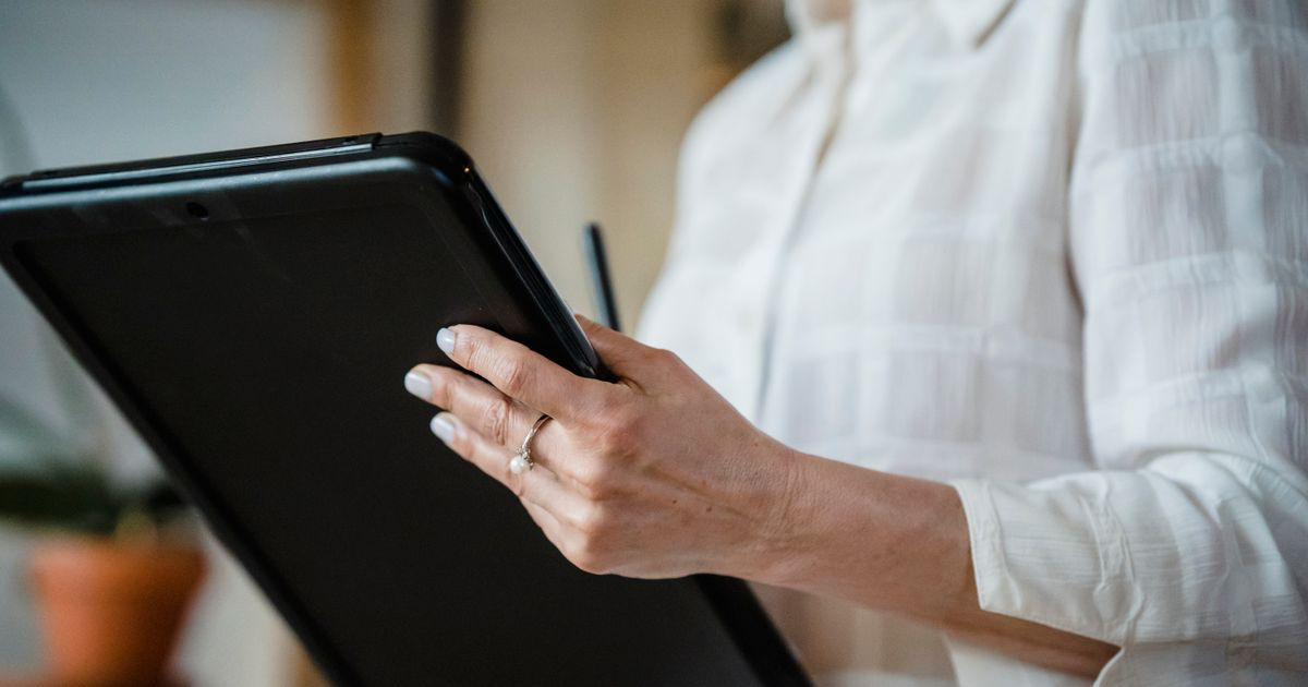 Manicured hand with white polish holding a tablet, illustrating how to edit nail photos on iPad