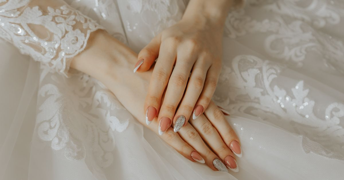 Close-up of a bride's hands with a long manicure resting on a lace wedding dress, the shape covered in how to photograph coffin nails