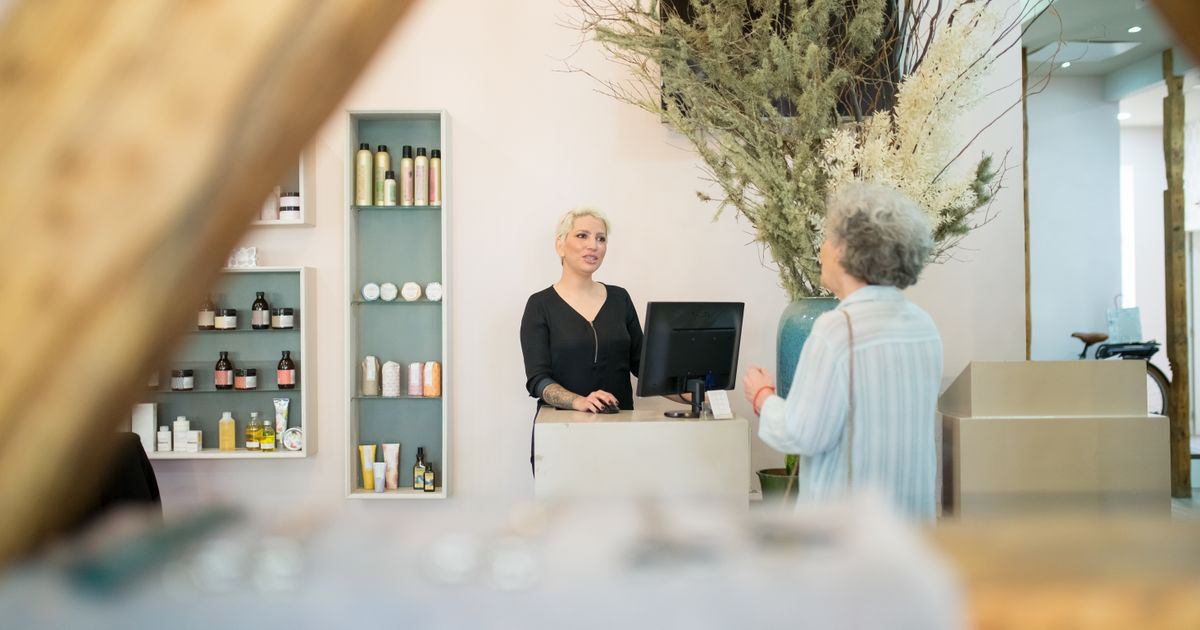 A client talking with a stylist at a salon reception desk, the kind of local business a nail tech markets in their own town