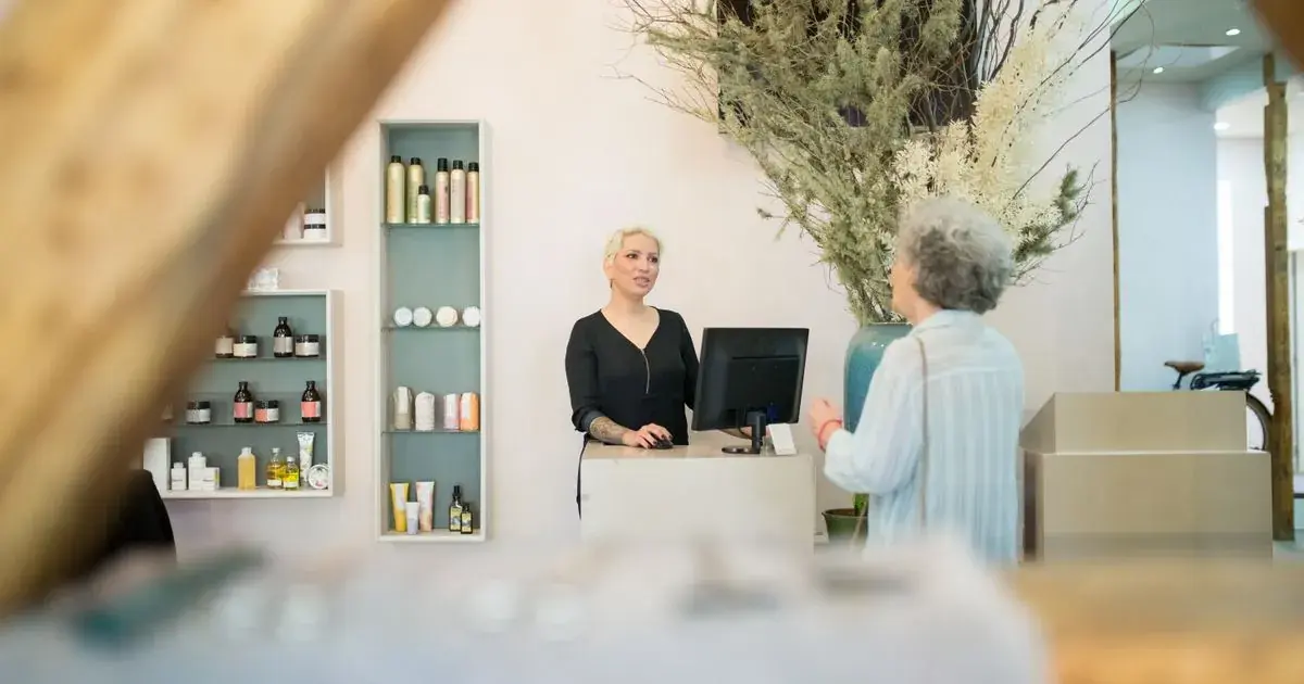 A client talking with a stylist at a salon reception desk, the kind of local business a nail tech markets in their own town