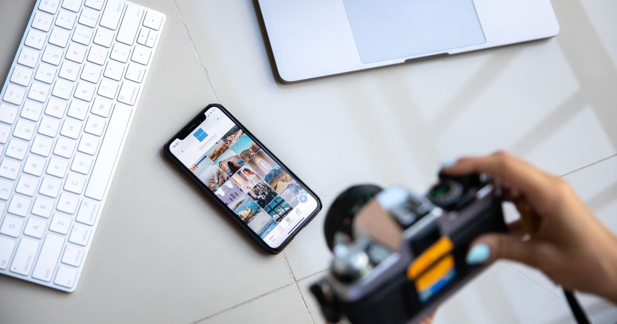 A smartphone, camera and laptop on a desk, the kind of setup used to edit nail photos in an app like Picsart
