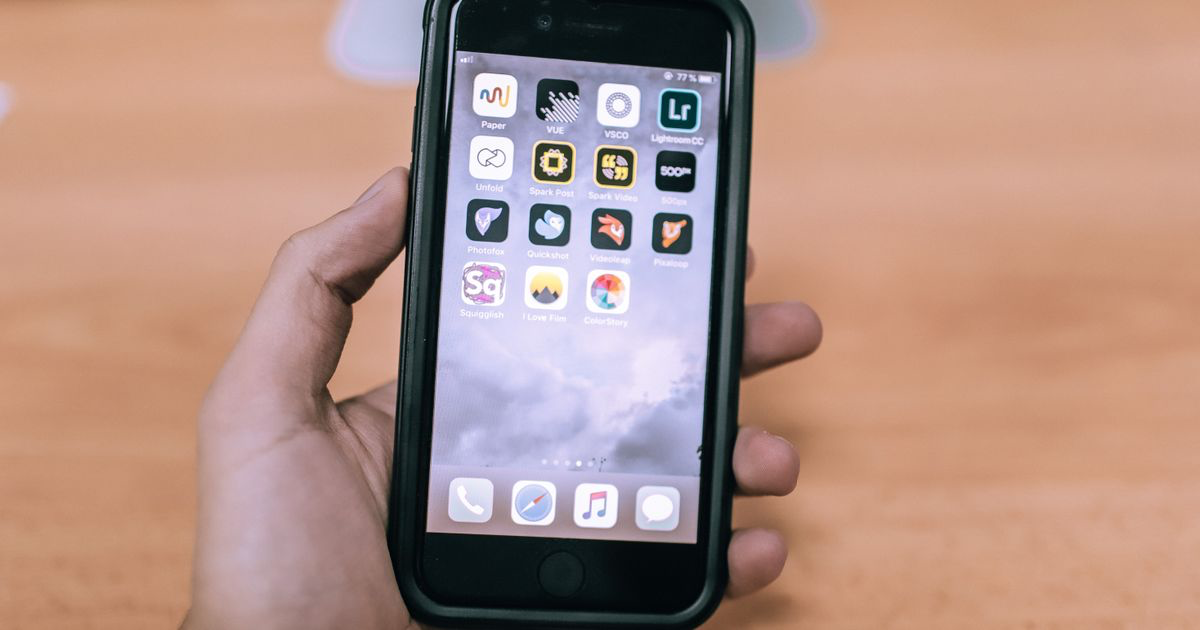A close-up of a hand holding a smartphone showing app icons, where AI photo editing tools for nail techs live