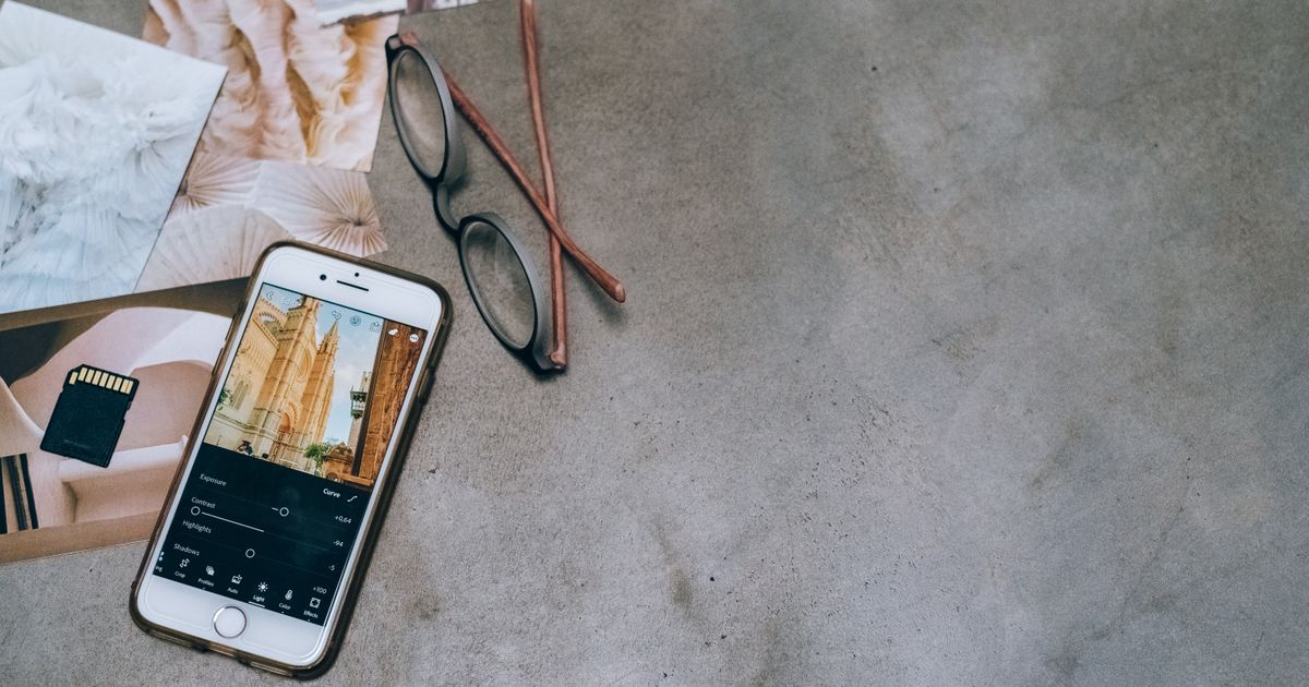 A smartphone, printed photographs and glasses laid out on a concrete surface, the kind of setup used for editing nail photos in Apple Photos