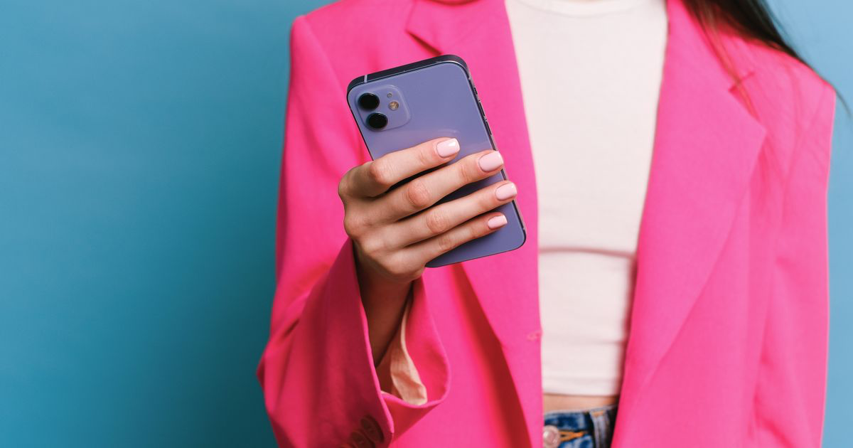 A woman in a pink blazer holding a smartphone, reviewing photos for a nail portfolio