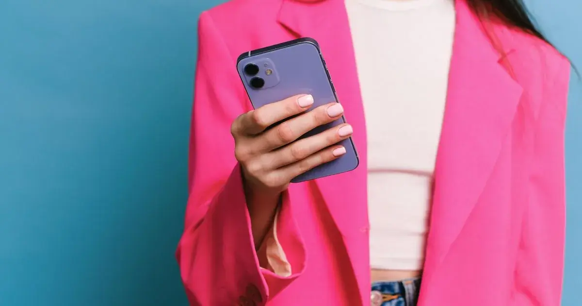 A woman in a pink blazer holding a smartphone, reviewing photos for a nail portfolio