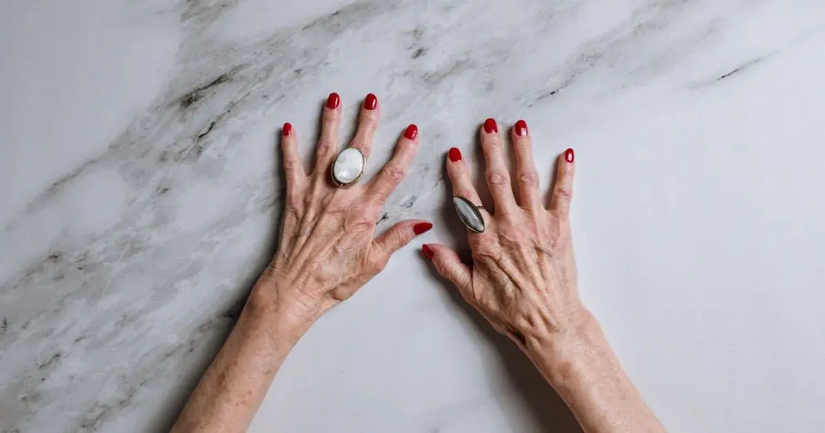 Two hands with red nails resting on a grey-veined marble surface, the stone pattern that marble nail photos have to reproduce on the nail