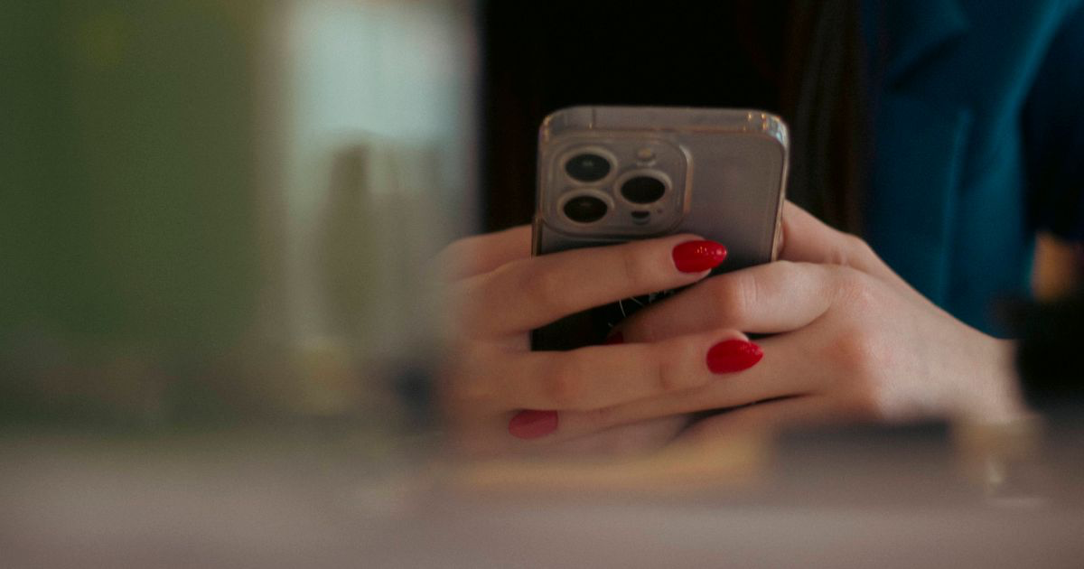 A close-up of a woman with red nails using a smartphone, the setup behind most nail photos edited for TikTok