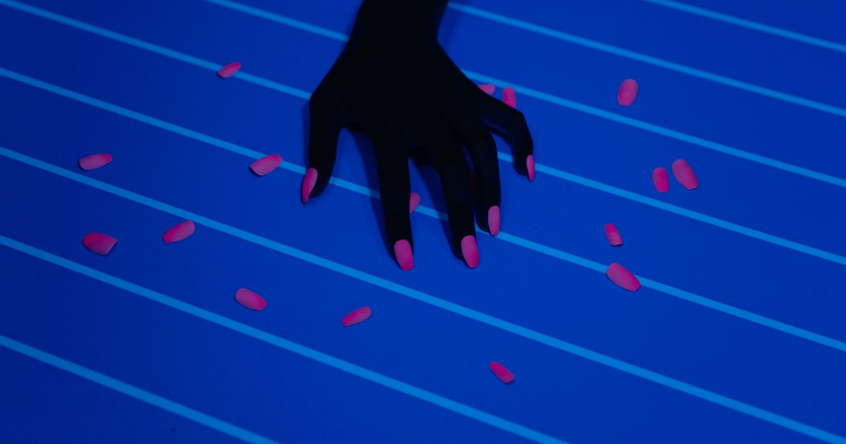 A hand with a brightly coloured manicure surrounded by nail polish bottles, the kind of neon set that clips in phone photos