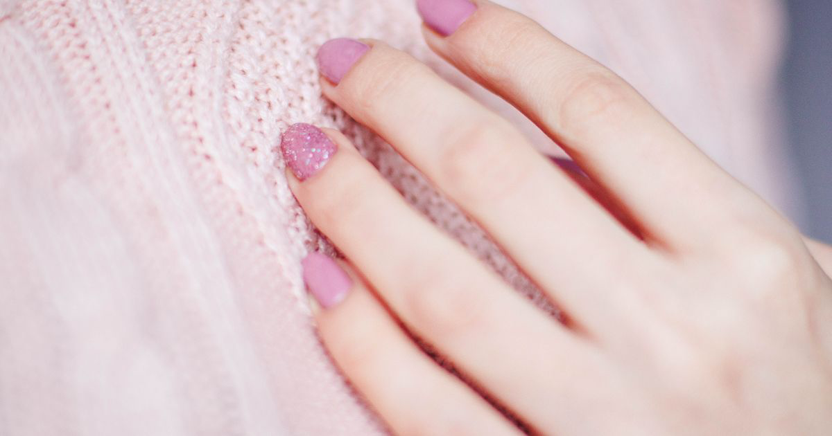 Close-up of a hand with a pink manicure resting on a knit sweater, the kind of shade covered in how to edit pink nail photos