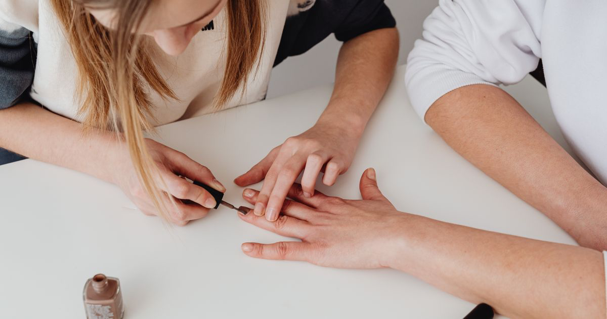 A nail technician painting a client's nails in a salon, the kind of setting covered in how to photograph almond nails