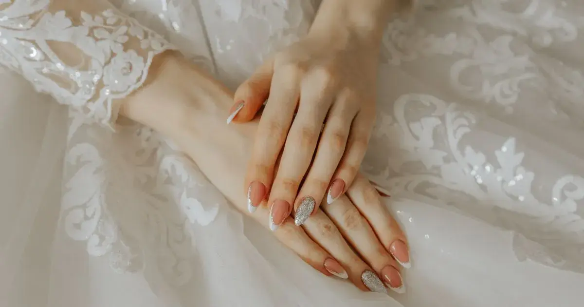Close-up of a bride's hands with a long manicure resting on a lace wedding dress, the shape covered in how to photograph coffin nails