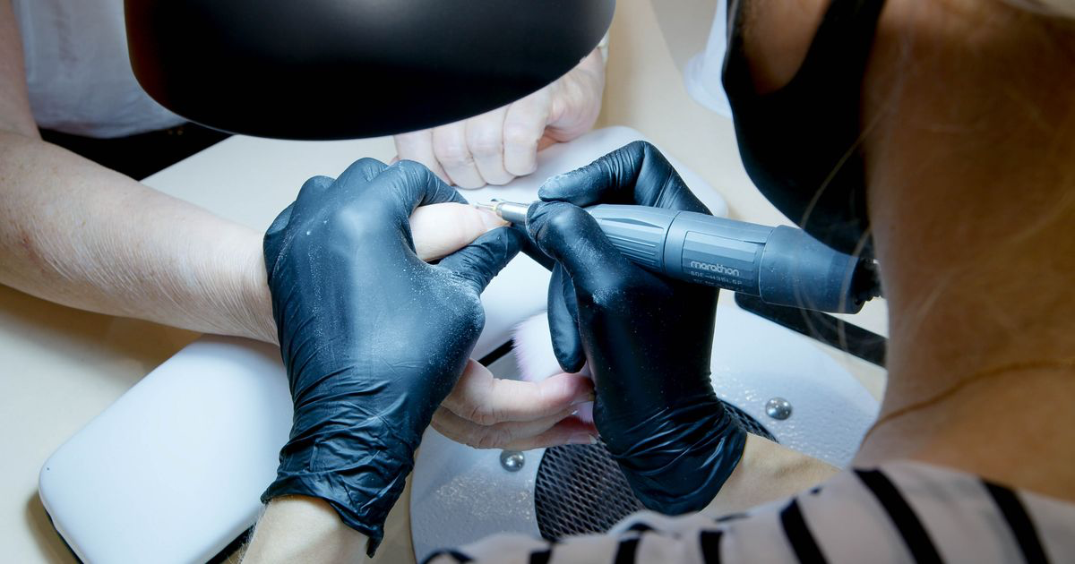 A manicurist working on a client's nails in a salon, illustrating how to refresh your nail portfolio