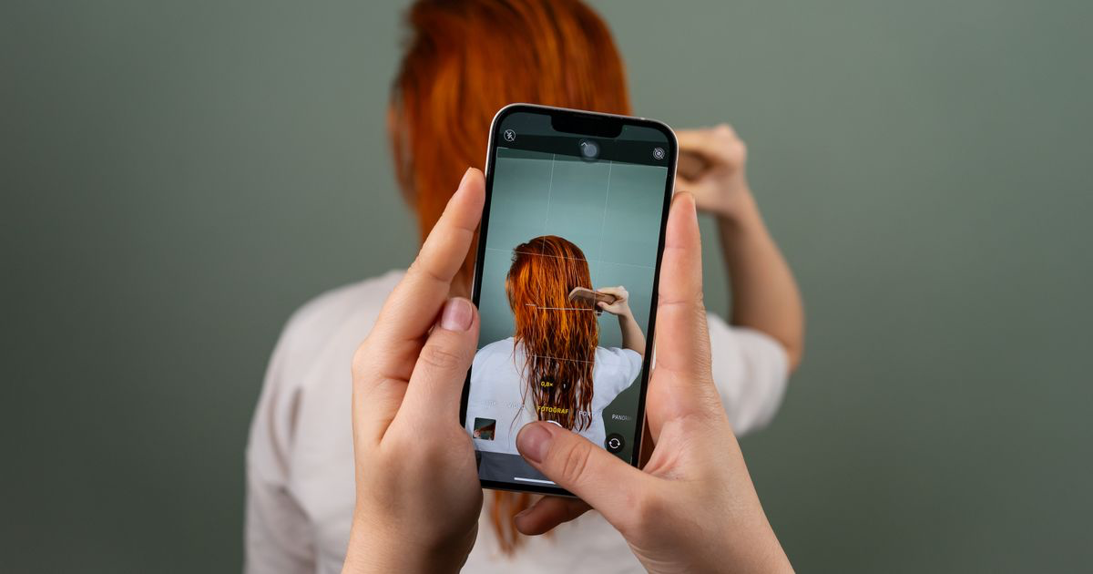 A person photographing someone on a smartphone indoors, illustrating how to resize nail photos for social media