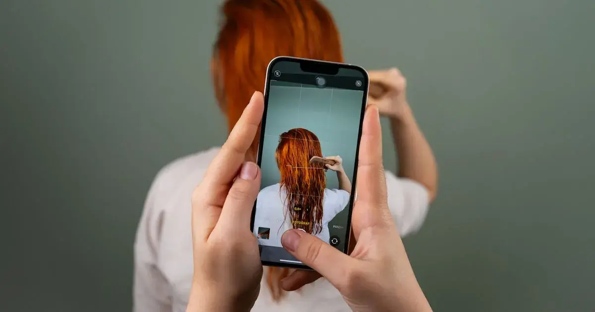 A person photographing someone on a smartphone indoors, illustrating how to resize nail photos for social media