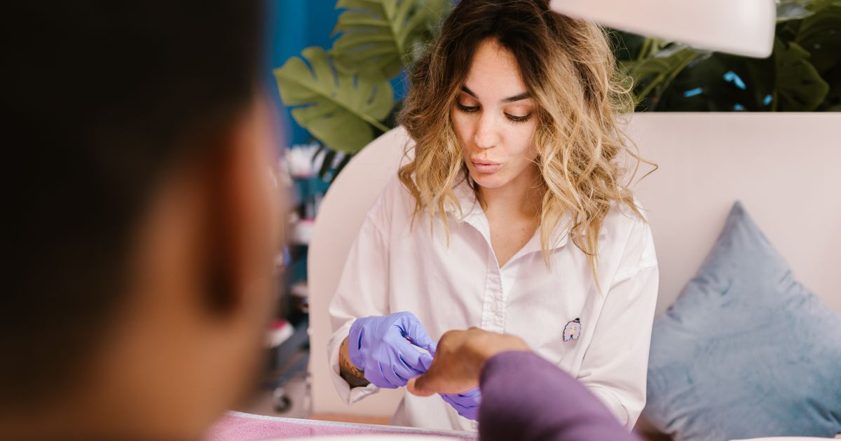 A nail technician working on a client's hands in a salon, the appointment where client retention is decided