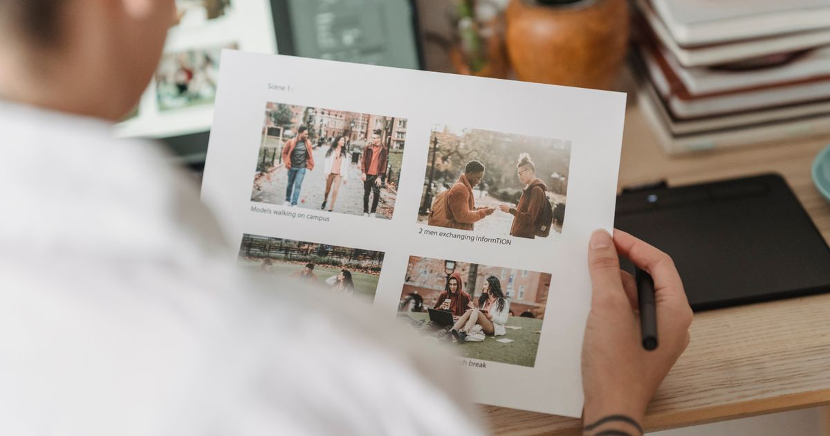 A photographer sorting printed photos at a table beside a laptop, the review step before deciding how to watermark nail photos