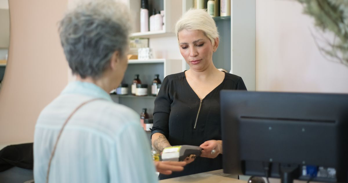 Client paying by card at a salon reception desk, the moment a nail deposit policy is applied