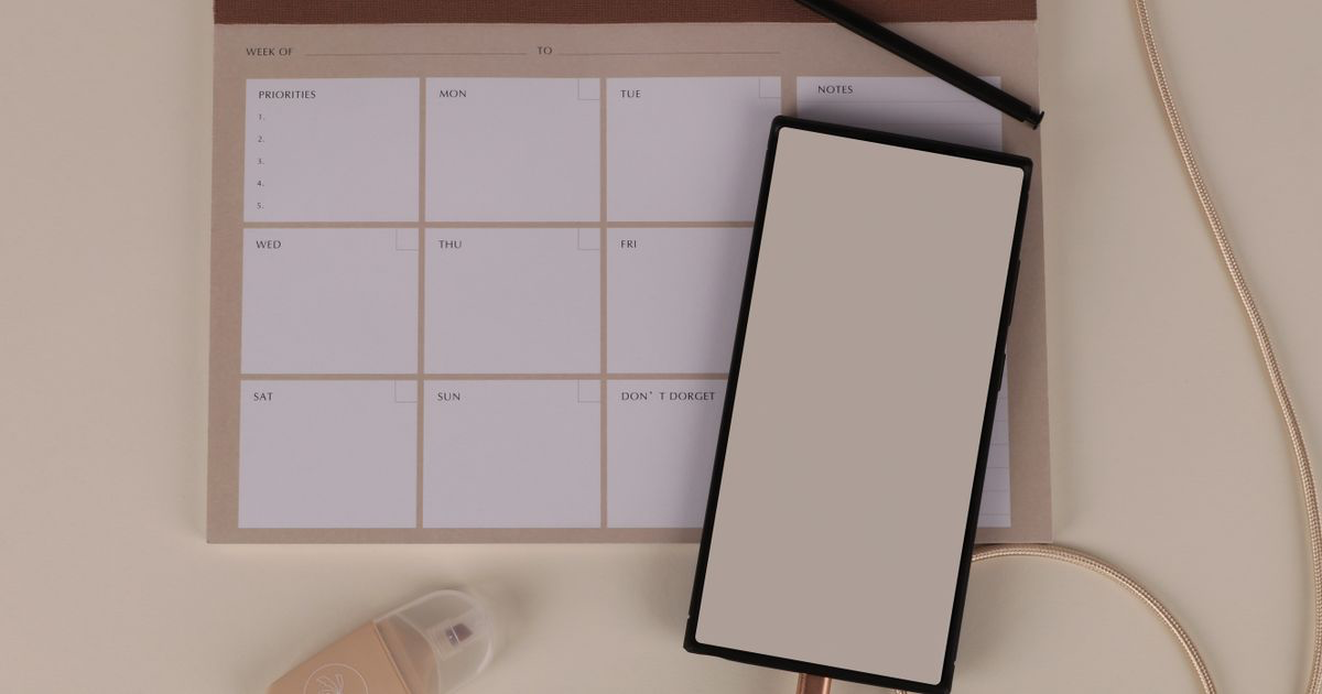 A weekly planner, smartphone and stationery on a desk, used to build a nail tech content calendar