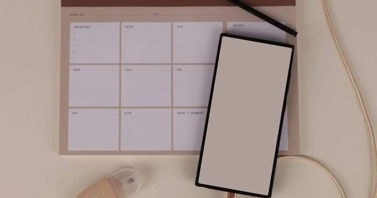 A weekly planner, smartphone and stationery on a desk, used to build a nail tech content calendar