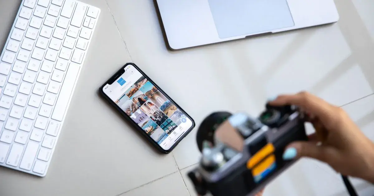 A smartphone, camera and laptop on a desk, the kind of setup used to edit nail photos in an app like Picsart